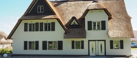 Une maison traditionnelle avec un toit de chaume, des murs blancs et des volets noirs.