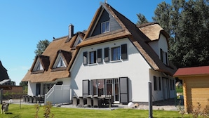 Ein Haus mit einem Strohdach, weißen Außenwänden und einer großen Rasenfläche.
