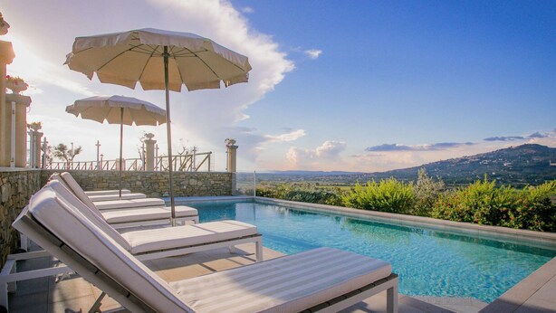 A pool area with lounge chairs and umbrellas, stone walls, and a view of the landscape. - Holiday Home in Cortona With Pool & Valley Views (Cortona)