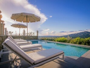 Ein Poolbereich mit Liegestühlen und Sonnenschirmen, Steinmauern und Blick auf die Landschaft.