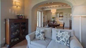 A living room with a white sofa, a wooden cabinet with glass doors, and a dining area in the background. - Holiday Home in Cortona With Pool & Valley Views (Cortona)
