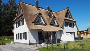 Ein modernes Haus mit einem markanten, dreieckigen Dach, großen Fenstern und einem gepflegten Rasen.