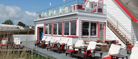 A boat with a white exterior and red trim, featuring outdoor seating with red cushions and a covered area with tables and chairs.