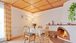Zona pranzo con camino in mattoni, sedie di legno, un tavolo con tovaglia bianca e un vaso di fiori.