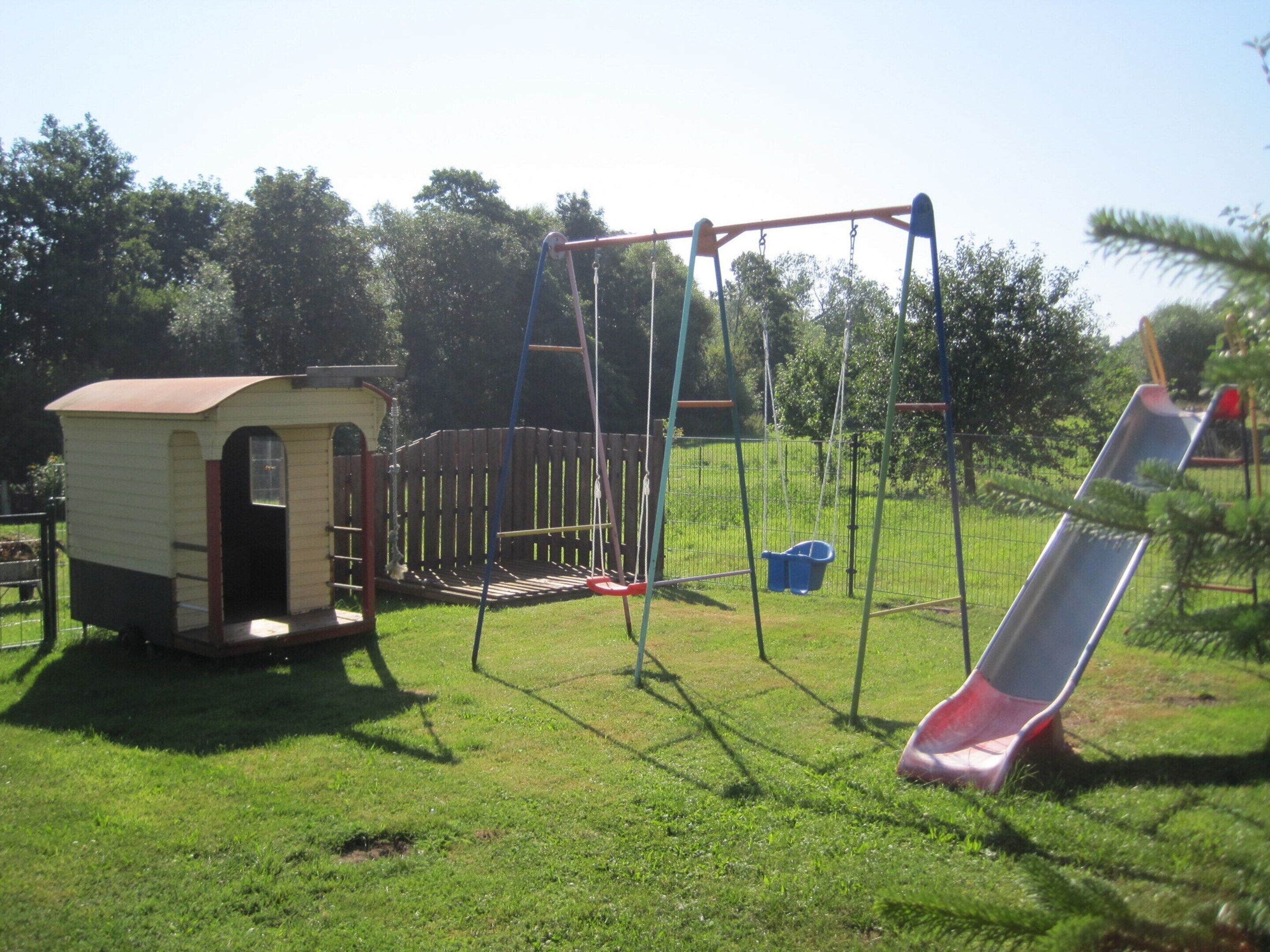A playground with a swing set, a slide, and a small shed.