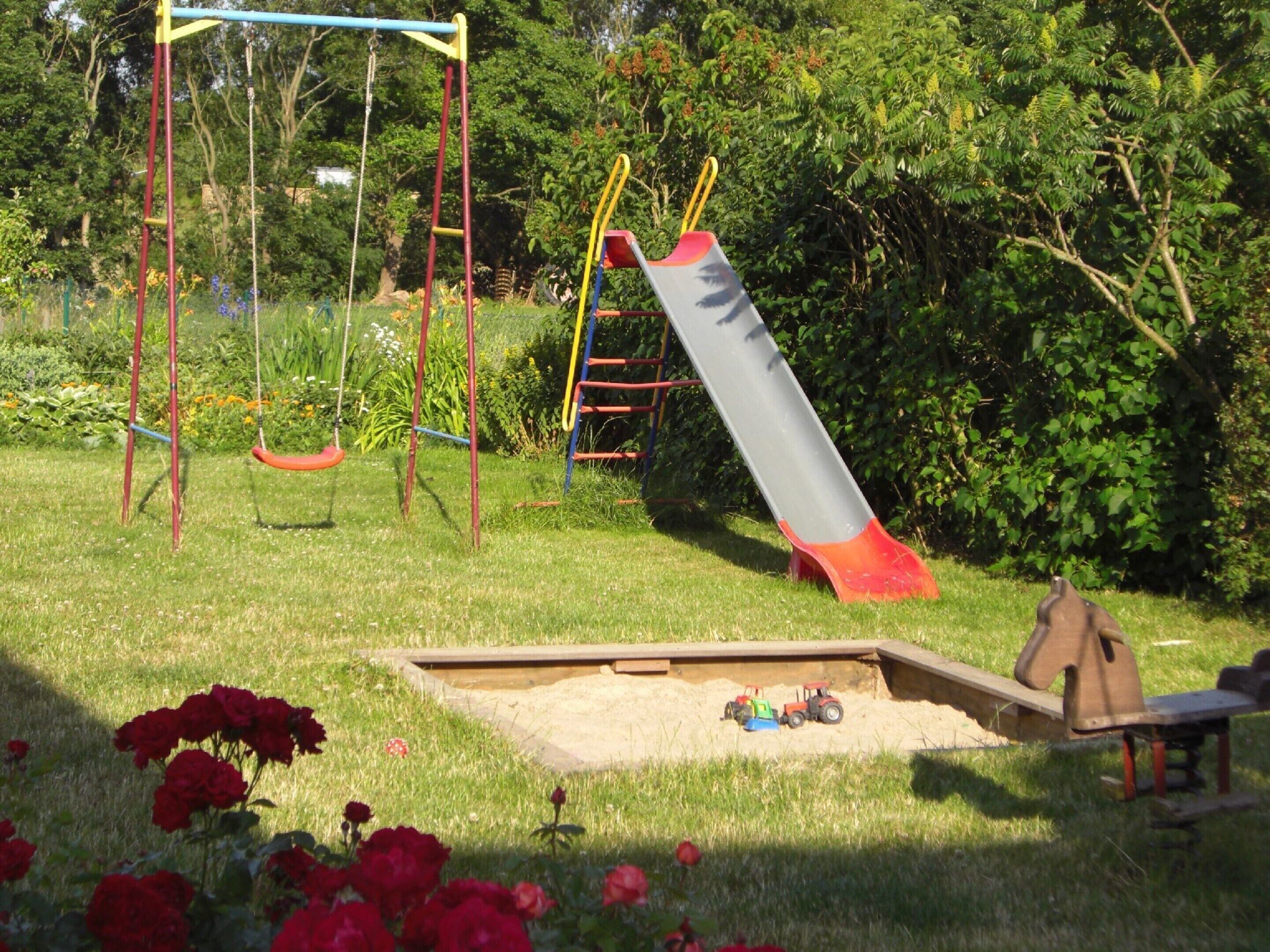 Ein Spielplatz mit Schaukeln, einer Rutsche und einem Sandkasten mit Spielzeugtraktoren.