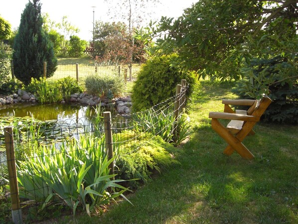 Un jardin avec un étang, un banc en bois et différentes plantes.