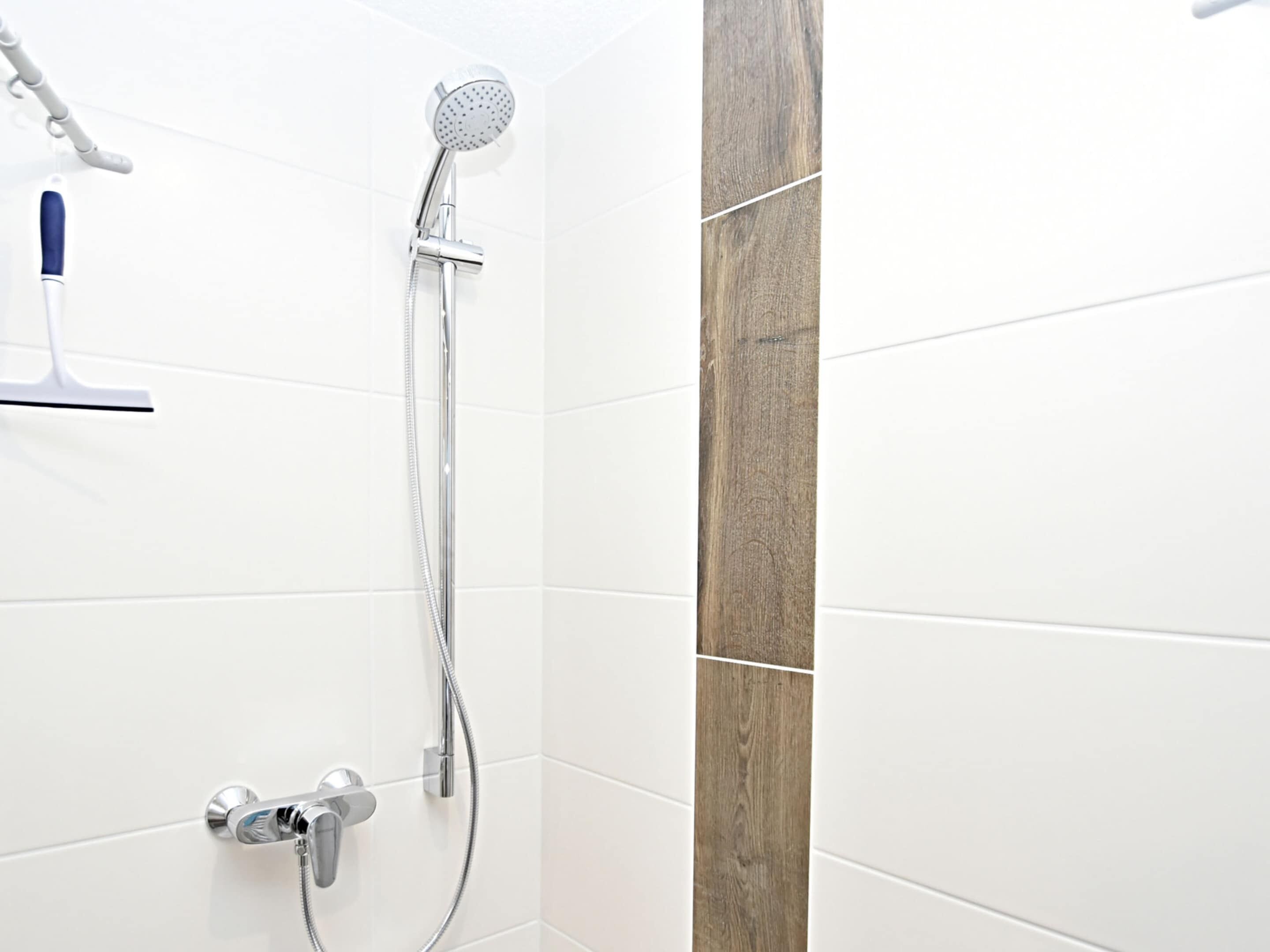 Un bagno con pareti piastrellate in bianco, una parete d'accento in legno, un soffione a mano e un rubinetto montato a parete.