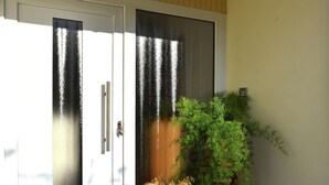 Uma porta de correr com painel de vidro fosco, um vaso de plantas e uma pequena mesa com um recipiente de flores.