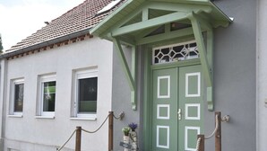 Un bâtiment avec une porte verte, des fenêtres à cadre blanc et un escalier en pierre menant à l’entrée.