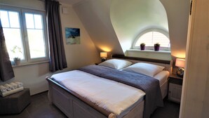 Een slaapkamer met een groot bed, een raam met gordijnen, een nachtkastje met een lamp en een klein raam met planten.