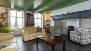 A living room with a beige sofa, a wooden coffee table, and plaid armchairs. There is a fireplace with a tiled wall behind it. - Scenic Holiday Home in Oostkapelle near Beach (Oostkapelle)