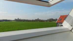 A view from a window with a skylight, overlooking a green field and a building with a red roof. - Scenic Holiday Home in Oostkapelle near Beach (Oostkapelle)