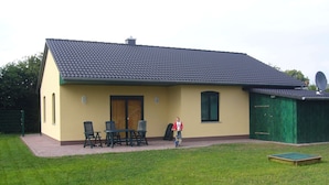 A single-story building with a tiled roof, a green garage, and a small patio area with outdoor furniture. - Gemutliche Ferienwohnung in Satow (Satow)