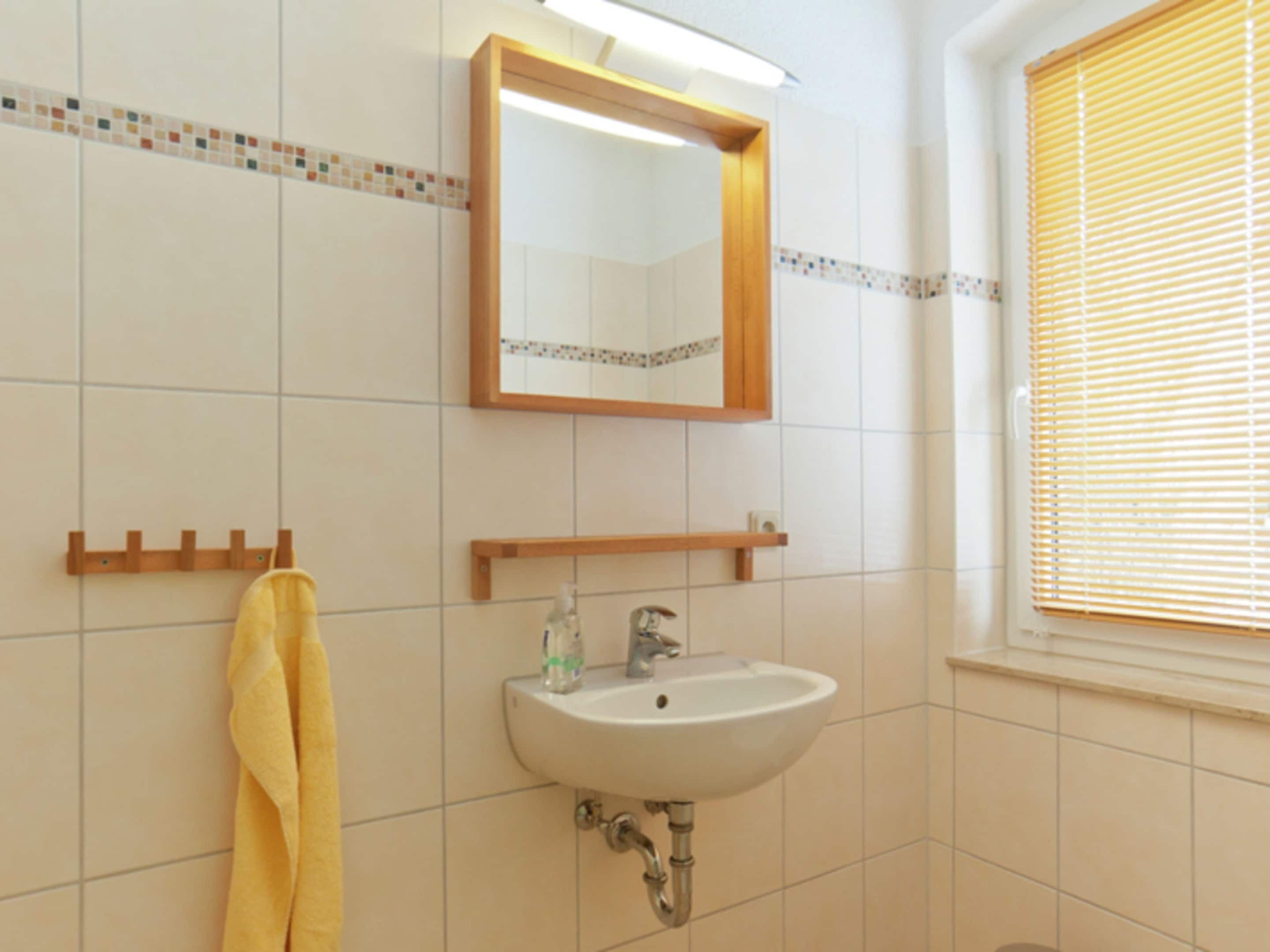 Un bagno con un lavandino bianco, uno specchio e un portasciugamani.