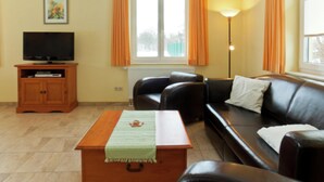 A living room with a sofa, a television on a wooden stand, a lamp, and a window with curtains. - Gemutliche Ferienwohnung in Satow (Satow)