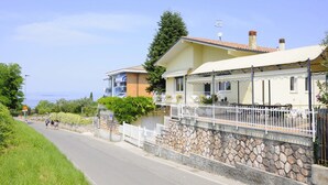 Ein Küstenhaus mit einer Steinwand, einem Balkon mit Gartenmöbeln und freiem Blick auf das Meer.