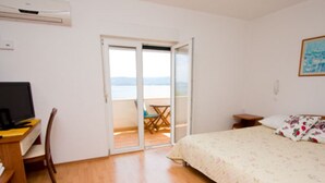 Une chambre à coucher comprenant un lit, un bureau avec un ordinateur, une chaise et une porte-fenêtre coulissante donnant sur un balcon équipé d’une table et de chaises.