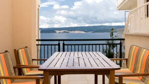 Un balcon avec une table en bois et des chaises à rayures, d’où l’on peut admirer un plan d’eau et un paysage lointain.