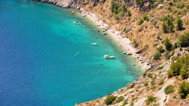 Un paysage côtier caractérisé par une eau turquoise et limpide, un terrain rocheux et une végétation clairsemée.