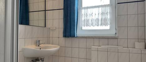A bathroom with a white sink, a mirror, a window with blue curtains, and a toilet.