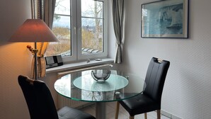 A dining area with a glass table, two chairs, a lamp, and a window with curtains. - Ferienwohnung in Zingst (Zingst)