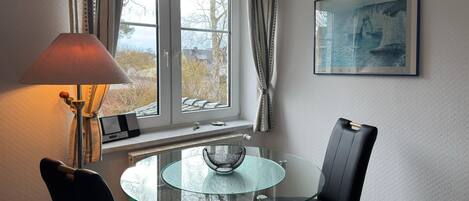 Un coin repas avec une table en verre, deux chaises, une lampe et une fenêtre avec des rideaux.