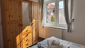 Ein Schlafzimmer mit Holzschrank, einem fenster mit Vorhängen, einer Heizung und einem Bett mit einem gefalteten Handtuch.