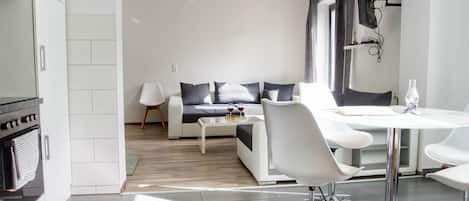 A modern kitchen with white cabinets, a built-in oven, and a dining area with a white table and chairs.