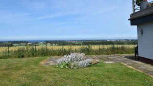 A rural landscape with a clear sky, a grassy area with a small bush, and a building with a metal structure on top. - Ferienwohnung in Bastorf for 3 Personen (Bastorf)