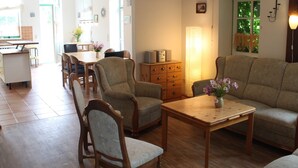 Ein geräumiges Wohnzimmer mit Couch, zwei Sesseln, einem Holztisch und einem Essbereich mit Tisch und Stühlen.