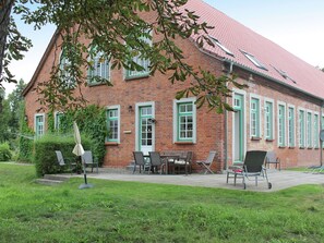 Ein Backsteinhaus mit grünen Fensterrahmen, einem roten Dach und einer Terrasse mit Gartenmöbeln.
