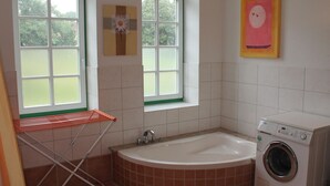 Ein Badezimmer mit einer Badewanne, einer Waschmaschine und einem Fenster mit Blick auf Grünfläche.