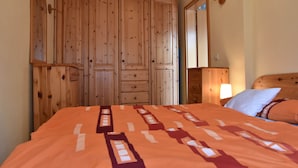 A bedroom with a large wooden wardrobe, a bed with an orange patterned bedspread, and a bedside lamp. - Attractive Bungalow in Damshagen near Sea (Damshagen)