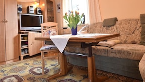 A cozy living room with a wooden TV stand, a sofa, a table with a vase of flowers, and a patterned rug. - Attractive Bungalow in Damshagen near Sea (Damshagen)