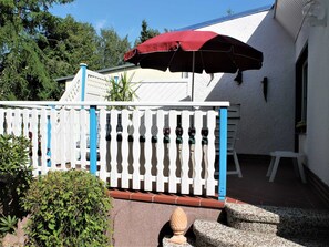 A patio area with a white picket fence, a red umbrella, and a white chair.