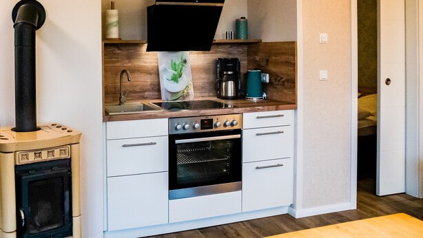 Una cocina compacta con estufa, horno, pileta y un extractor de aire negro.