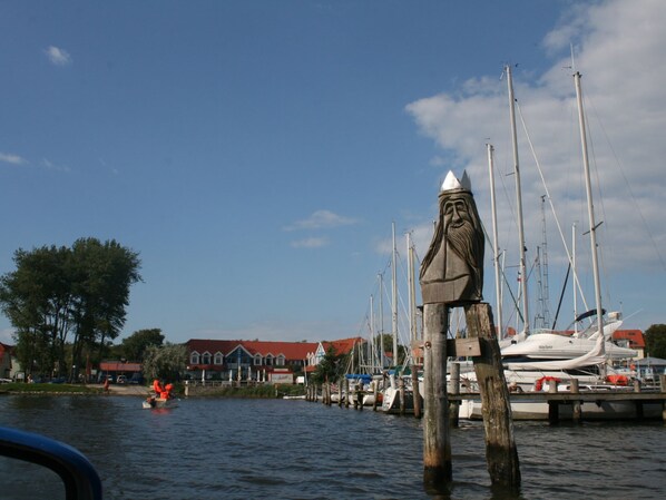 Ein Yachthafen mit angestaubten Booten, ein hölzerner Pfosten mit einer Statue und ein Gebäude mit rotem Dach im Hintergrund.
