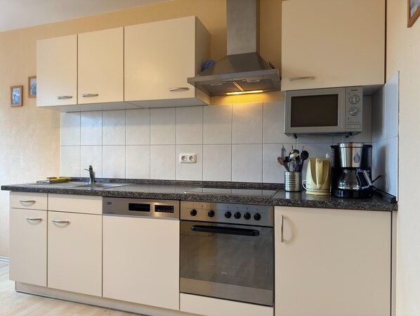 A modern kitchen with white cabinets, a stainless steel oven, a built-in microwave, and a coffee maker. - Wiek Apartment With Garden (Wiek)