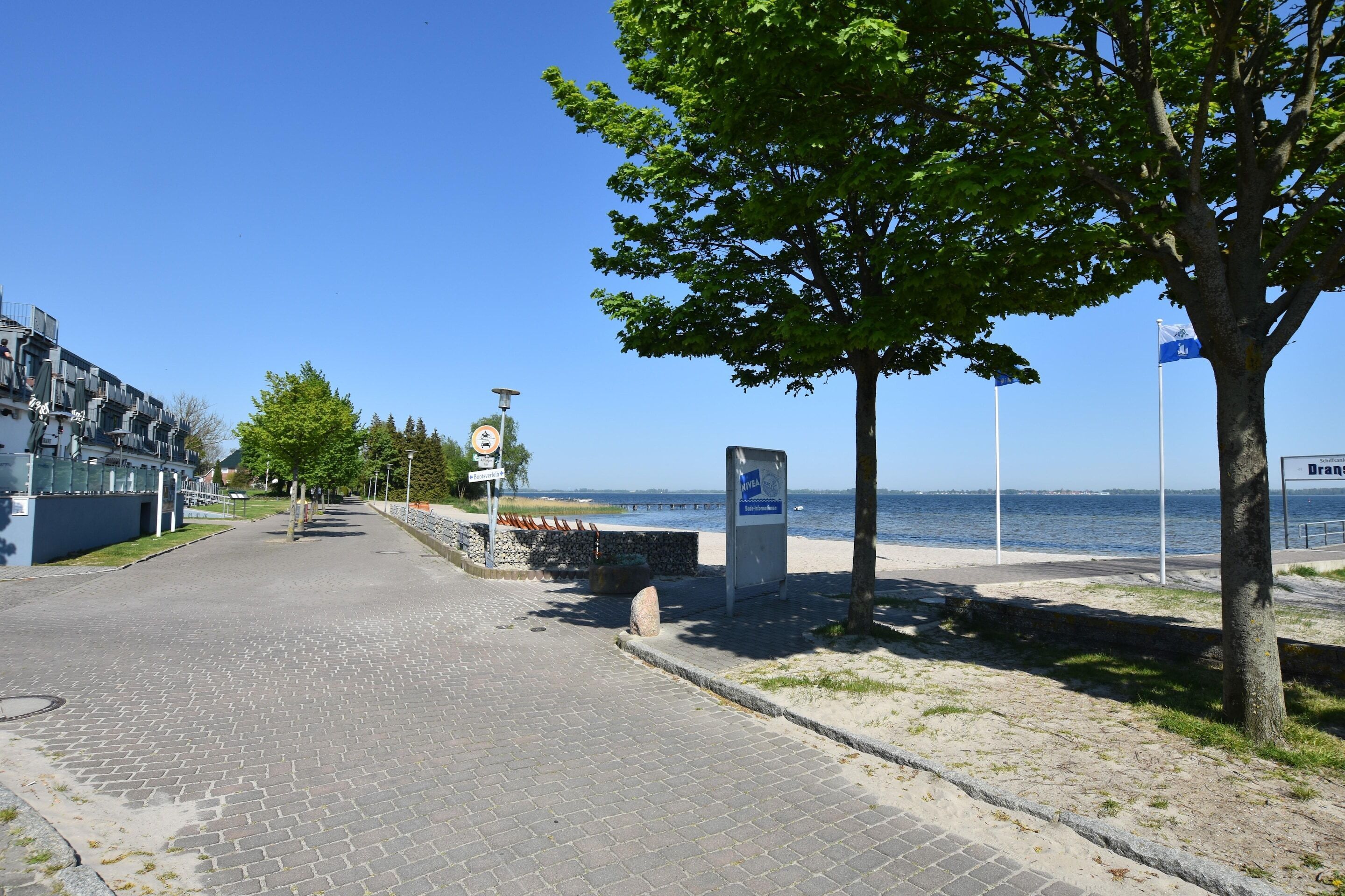 Ein gepflasterter Weg führt zu einem Strand, mit einem Schild, das einen Aussichtspunkt kennzeichnet.
