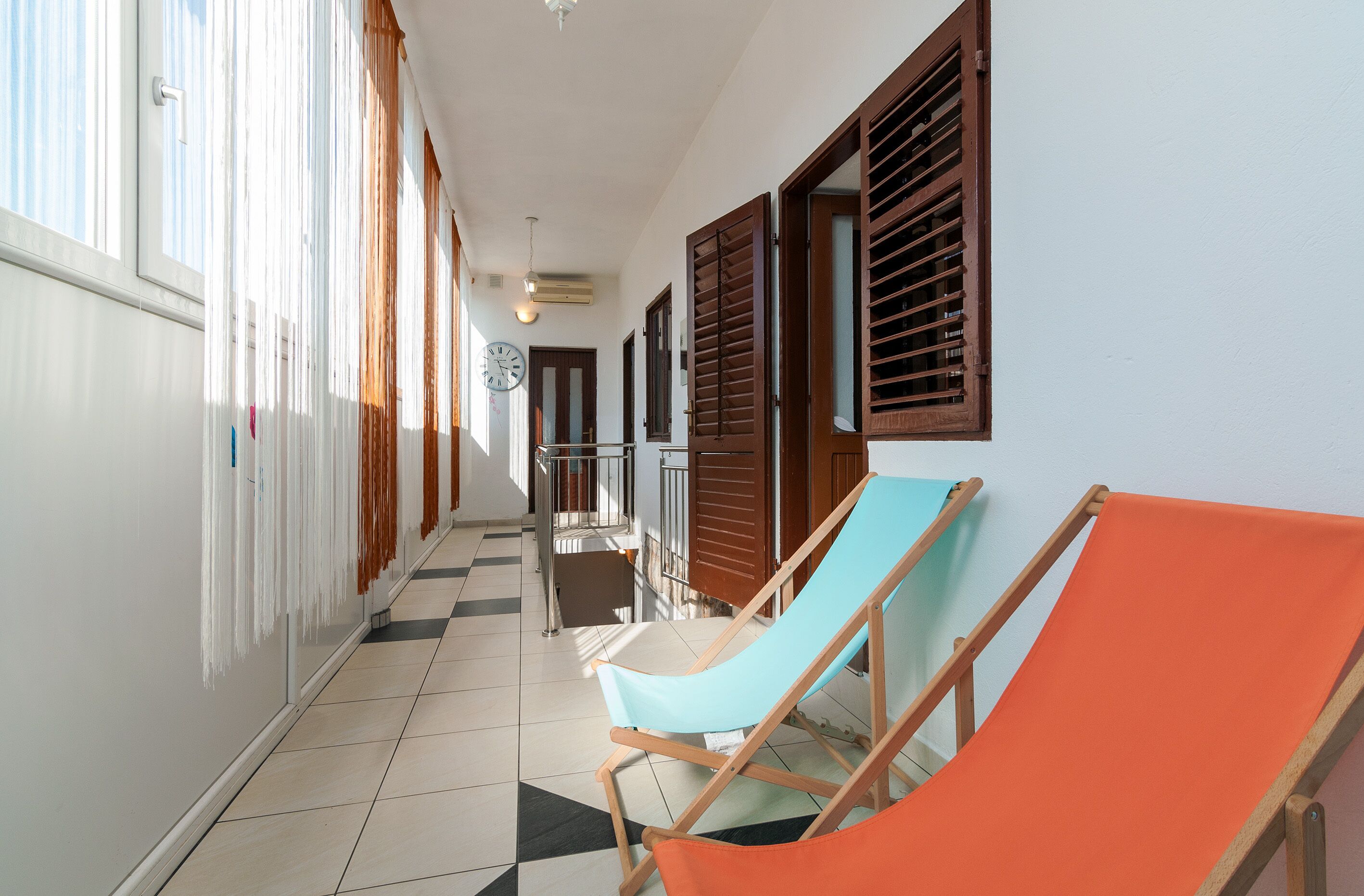 A corridor with wooden shutters, a tiled floor, and two beach chairs.