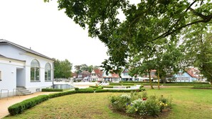 A courtyard with a white building, a bench, and a flower bed. - Spacious Bungalow near Sea in Grundshagen (Klütz)