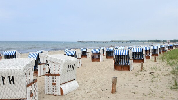 Beachside beach chairs with striped awnings, a sandy beach, and a pier in the background. - Spacious Bungalow near Sea in Grundshagen (Klütz)