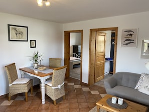 A dining area with a table and chairs, a sofa, and a bed in the background.