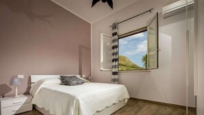 Quarto com cama, mesas de cabeceira, abajur e janela com vista para uma montanha.