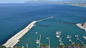 Vista aérea de uma marina costeira com barcos atracados, um molhe e uma cordilheira ao longe.