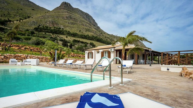 Área de piscina com espreguiçadeiras, piscina e montanhas ao fundo.