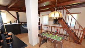 Una habitación amplia con una escalera de madera, una mesa de fútbol de mesa y una mesa negra con tazas.