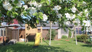 A playground with a slide and swings, surrounded by a grassy area and trees. - Strandbungalow, Boltenhagen (Boltenhagen)