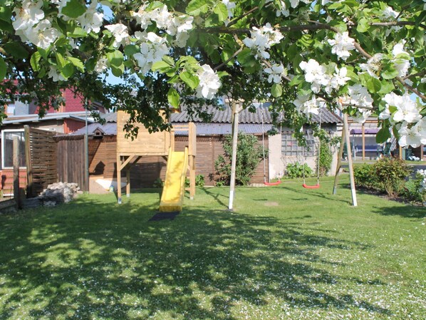 A playground with a slide and swings, surrounded by a grassy area and trees. - Strandbungalow, Boltenhagen (Boltenhagen)